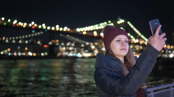 Mujer joven se sienta en Brooklyn Bridge Nueva York por la noche — Foto de Stock