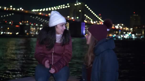 Dos chicas se relajan en Brooklyn Bridge New York por la noche — Vídeo de stock