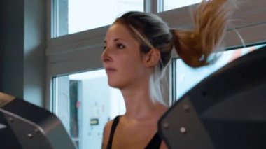 Kız spor salonunda koşu bandında koşuyor.