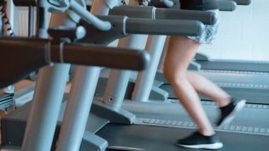 Kız spor salonunda koşu bandında koşuyor.