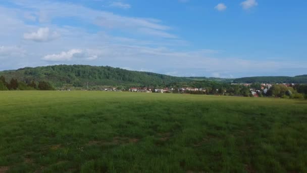 Amplia vista angular sobre un campo verde y un pequeño pueblo - vuelo aéreo con drones — Vídeo de stock