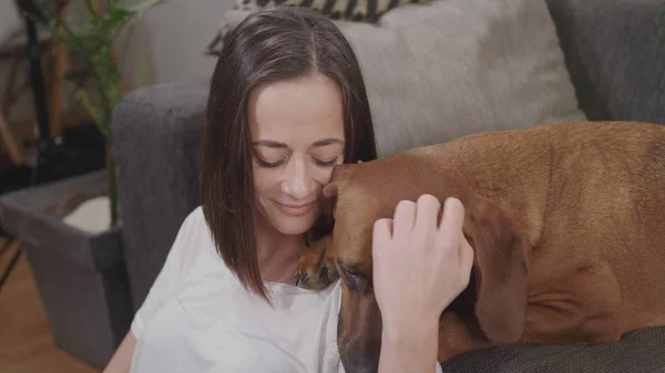 Young woman pets her dog while relaxing in the living room