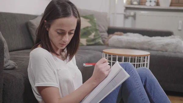 Young woman writes some notes while sitting on the floor in her living room