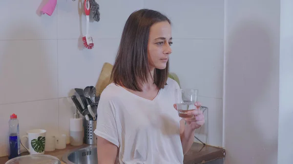 Young sporty woman drinks clear fresh water in the kitchen — Stock Photo, Image