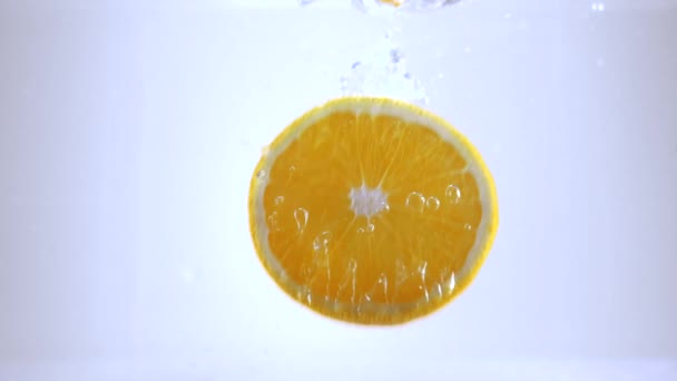 Orangenscheiben fallen in Zeitlupe ins Wasser — Stockvideo