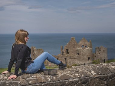 Kız Kuzey İrlanda Dunluce Kalesi'nde duvarda rahatlatır 