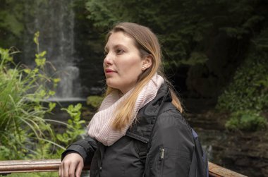 İrlanda 'da bir şelalenin önündeki genç kadın.