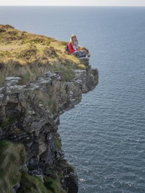 Young woman sitting on the edge of a cliff at the Irish west coast - travel photography clipart
