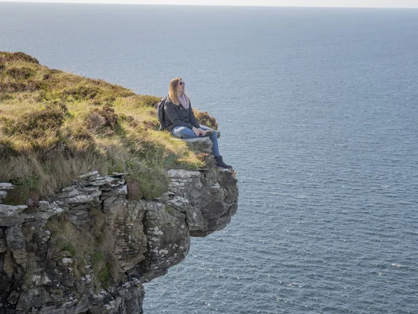 Reckless woman sitting on the edge of a cliff at the Irish west coast - travel photography