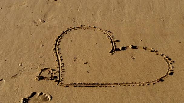 女の子はビーチで砂の中にハートのシンボルを書きます — ストック動画