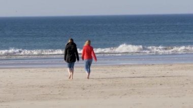 İki kız sonbaharda soğuk bir günde Kuzey İrlanda'da kumlu plaj boyunca yürümek  