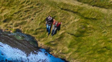 İrlanda kıyılarının kayalıklarında çimenlerde yatan iki kız - yukarıdan drone görünümü - seyahat fotoğrafçılığı