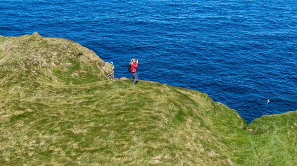 Two girls in Ireland walk on the cliffs of Kilkee on a sunny day - aerial drone view