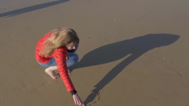 Девушка пишет символ сердца на песке на пляже — стоковое видео