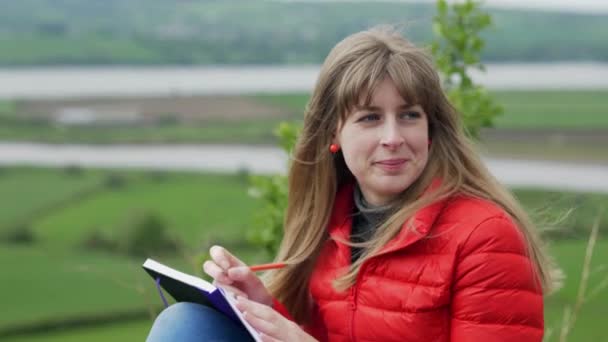 Jeune femme écrit des notes tout en étant assis dans la nature verte de l'Irlande 