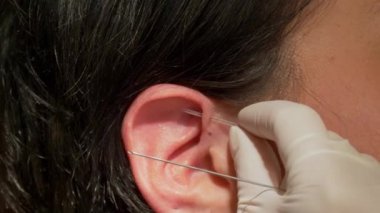 Kadın kulağına piercing taktırıyor. Yakın mesafeden piercing taktırıyor.