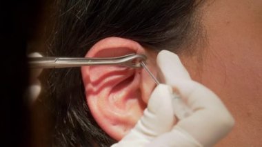 Kadın kulağına piercing taktırıyor. Yakın mesafeden piercing taktırıyor.