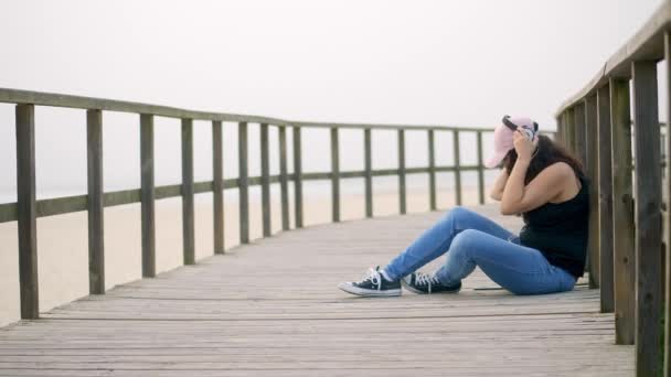 若い女性はビーチで木製の桟橋に座っています スローモーションショット — ストック動画