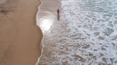 Bikinili seksi bir kadın okyanusta kumlu bir sahilde yürüyor. Hava aracı görüntüleri.