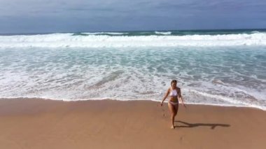 Bikinili seksi bir kadın okyanusta kumlu bir sahilde yürüyor. Hava aracı görüntüleri.