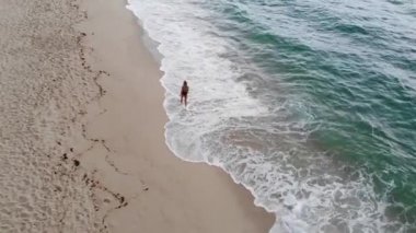 Mayolu seksi bir kız okyanustaki kumlu bir sahilde yürüyor. Hava aracı görüntüleri.