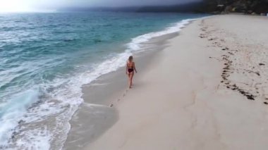 Okyanusun kumlu sahilinde tek başına güzel bir kız. Hava aracı görüntüsü.
