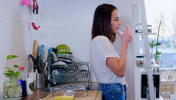 Young sporty woman drinks clear fresh water in the kitchen — Stock Photo, Image