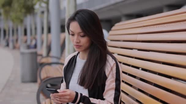 Jovem mulher asiática escreve mensagens de texto em seu telefone — Vídeo de Stock