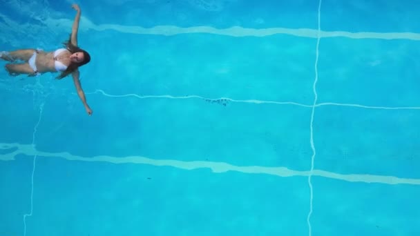 Νεαρή γυναίκα απολαμβάνει το κολύμπι στο δροσερό νερό μιας πισίνας το καλοκαίρι — Αρχείο Βίντεο