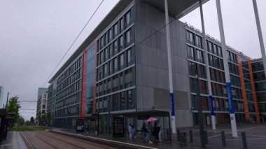 LUXEMBOURG, EUROPE - 1 Eylül 2025 - İnsanlar yağmurlu bir günde Kirchberg iş bölgesinde modern bir tramvay istasyonunda toplu taşıma bekliyorlar