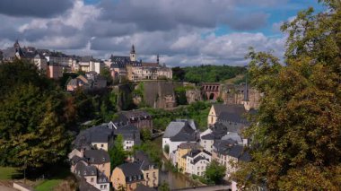 Lüksemburg 'un panoramik manzarasında Grund bölgesi, Alzette Nehri ve bulutlu gökyüzünün altında Neumunster Manastırı yer almaktadır.