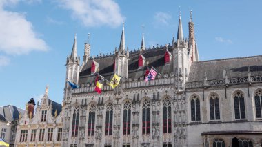 BRUGES, BELGIUM - 15 Eylül 2025 - Bruges Belediye Binası cephesinde mavi gökyüzüne karşı bayraklar ve gotik mimari ayrıntılar gösteriliyor