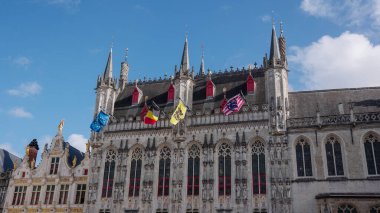 BRUGES, BELGIUM - 15 Eylül 2025 - Bruges belediye binası mavi gökyüzünün altında duruyor, bayraklar sergileniyor, tarihi Avrupa mimarisi