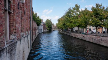 BRUGES, BELGIUM - 15 Eylül 2025 - Bruges kanal suyu tarihi mimari, yeşil ağaçlar ve mavi gökyüzünü yansıtıyor