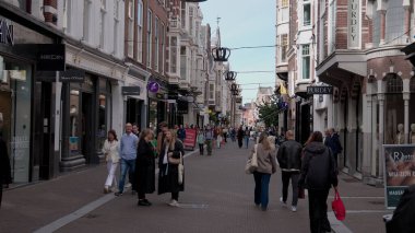 HAGUE, NETHERLANDS - 14 Eylül 2025 - Yayalar, taç süslemeleri ve tarihi mimariyle süslenmiş canlı bir alışveriş caddesi boyunca yürüyorlar.