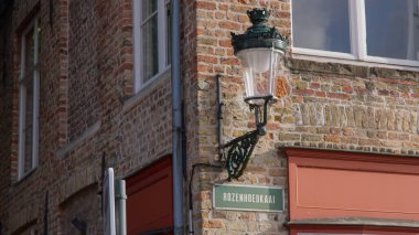 BRUGES, BELGIUM - 15 Eylül 2025 - Brüj 'deki Rozenhoedkaai' deki tuğla bina köşesini aydınlatan dekoratif sokak lambası