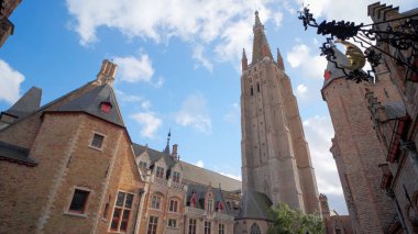 BRUGES, BELGIUM - 15 EYLÜL 2025 - Bruges caddesi üzerinde tarihi tuğla binalar ve Meryem Ana Kulesi Kilisesi 'nin mavi gökyüzüne uzandığı