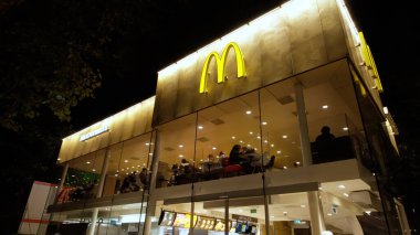ROTTERDAM, NETHERLANDS - 13 Eylül 2025 - Modern McDonald 's fast food restoranı geceleri parlarken ve insanlar içeride yemek yerken