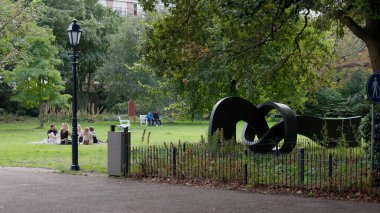 HAGUE, NETHERLANDS - 14 Eylül 2025 - Hollanda, Lahey 'deki yeşil bir parkta boş zamanların ve soyut bir heykelin keyfini çıkaran insanlar