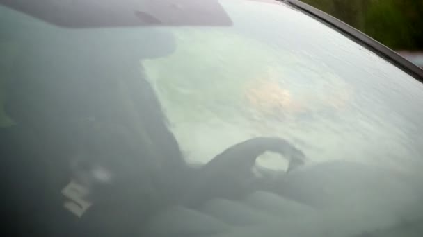 Starkregen, Schauer, Tropfen fallen auf die Windschutzscheibe eines leeren Autos, das auf dem Parkplatz steht. Durch das nasse Glas sieht man das Lenkrad und den leeren Fahrersitz. — Stockvideo