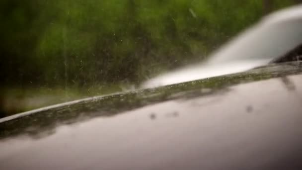 Blick von außen, heftiger Regen, Schauer, Tropfen fallen auf die Motorhaube eines leeren schwarzen Autos, das auf dem Parkplatz steht. Tröpfchen fließen in kleinen Bächen über die Motorhaube — Stockvideo