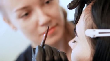 yakın çekim. Genç kadın kaş düzeltme yordamı alır. kosmetolog Šminker siyah lastik eldiven kaşları Güzellik salon üzerinde boya fırça ile uygulanır. Yüz için profesyonel bakım.