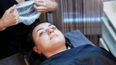 Güzellik Salonu. kirpik uzatma yordamı. Asıl müşteri ile özel bir tek kullanımlık kap elbise, tüm saç temizler, istemci yordam için hazırlar