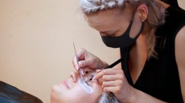Güzellik Salonu. kirpik uzatma için yordam. Yüzündeki bandaj master her cilium özel tutkalla yapıştırmış, iki cımbız ile çalışır