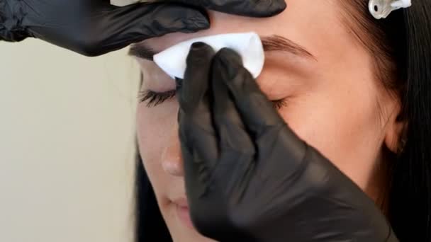 Beauty saloon. a close-up, the master wipes the eyebrow area with a cotton disc moistened with antiseptic — Stock Video