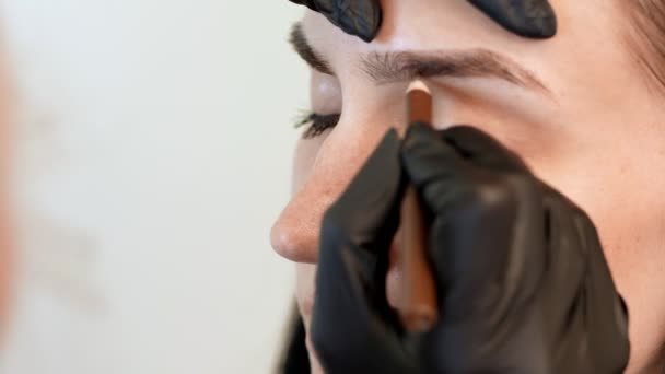 Beauty saloon. Eyebrow correction. close-up, cosmetologist, browmaker, master in black gloves, draws with special pencil the shape of eyebrows before applying eyebrow dye — Stock Video