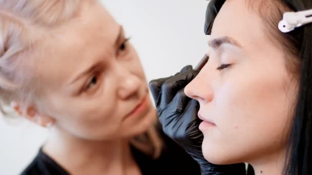 Beauty saloon. Eyebrow correction. cosmetologist, browmaker, master in black rubber gloves, draws with special pencil the shape of eyebrows before applying eyebrow dye — Stock Video