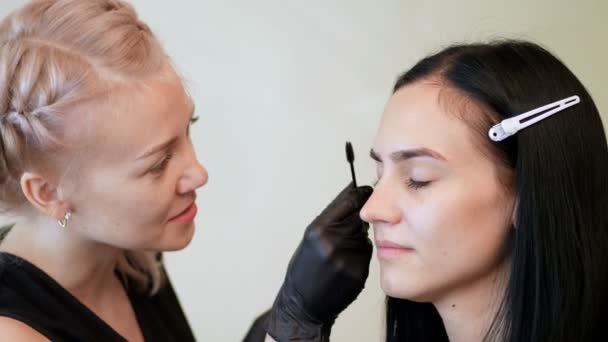 Salão de beleza. o cosmetician em luvas de borracha pretas guarda uma escova especial e penteia sobrancelhas. Mestre corrige a forma das sobrancelhas. Cuidados profissionais para o rosto . — Vídeo de Stock