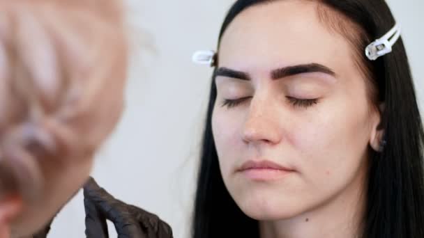 Salon de beauté. close-up, esthéticienne en gants de caoutchouc noir, peigne délicatement les sourcils du client avec une petite brosse spéciale, peigne, façonne les sourcils après coloration — Video