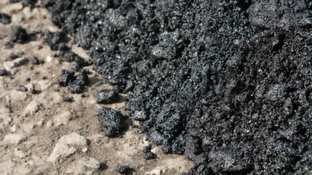 Close-up, asfalto fresco no processo de colocação na estrada, grandes pedaços, em resina, preto, brilha ao sol , — Vídeo de Stock